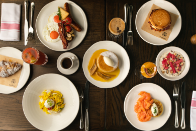 Six plates of brunch food, coffee, knife, fork