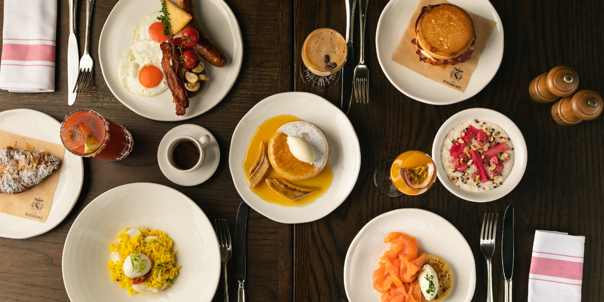 Six plates of brunch food, coffee, knife, fork